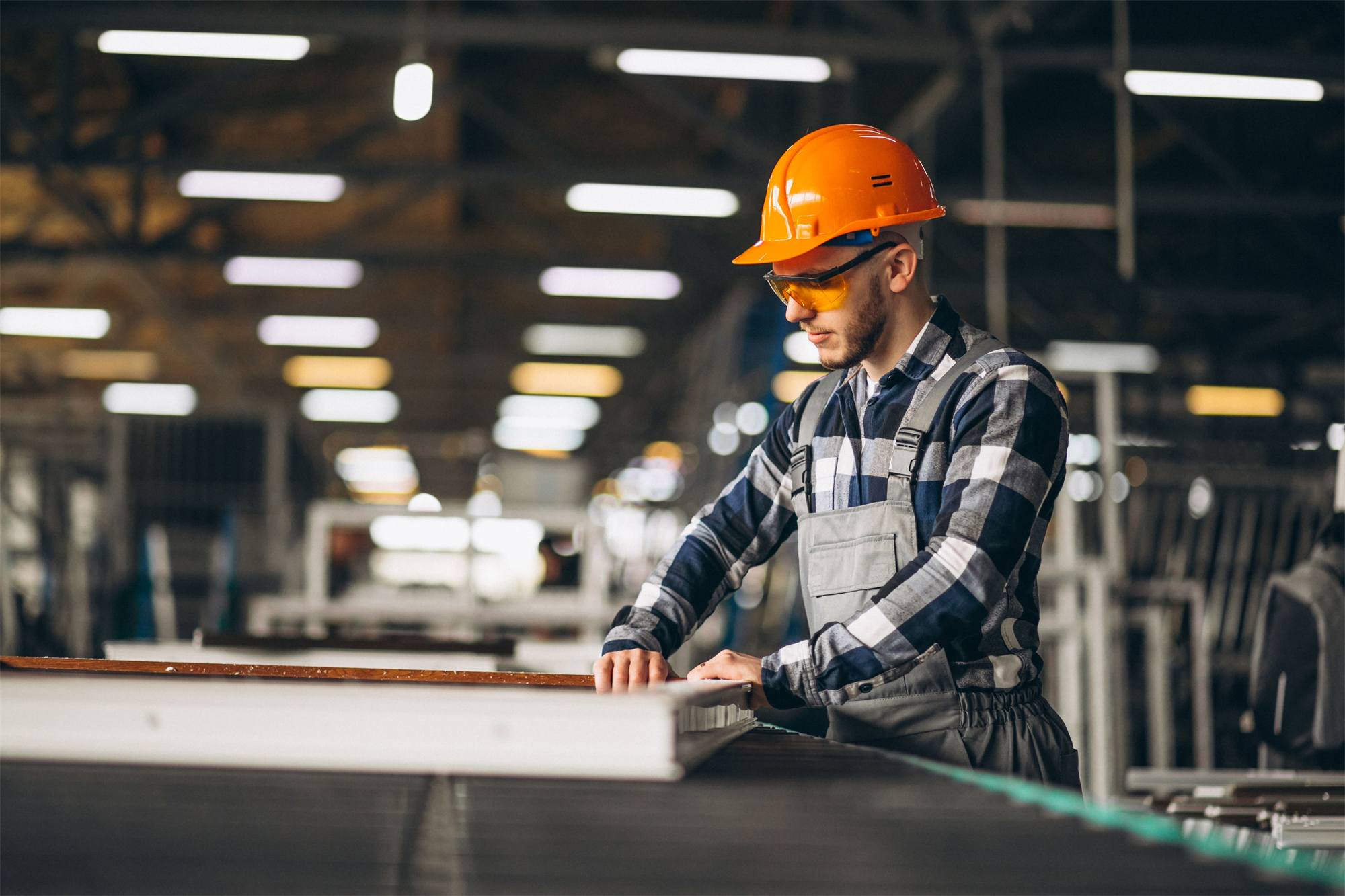 Profissional com capacete e óculos de proteção conferindo painéis metálicos em ambiente industrial